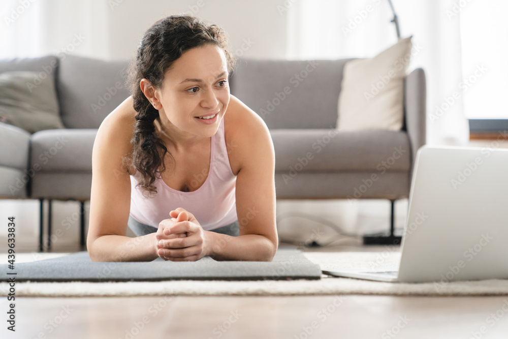 Close up portrait of a caucasian fitness woman exercising at home on mat standing in plank position using laptop as a tutorial. Training at home Close up portrait of a caucasian fitness woman exercising at home on mat standing in plank position using laptop as a tutorial. Training at home