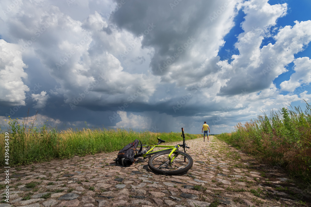 traveling on a bicycle, a man looks at a thunderstorm