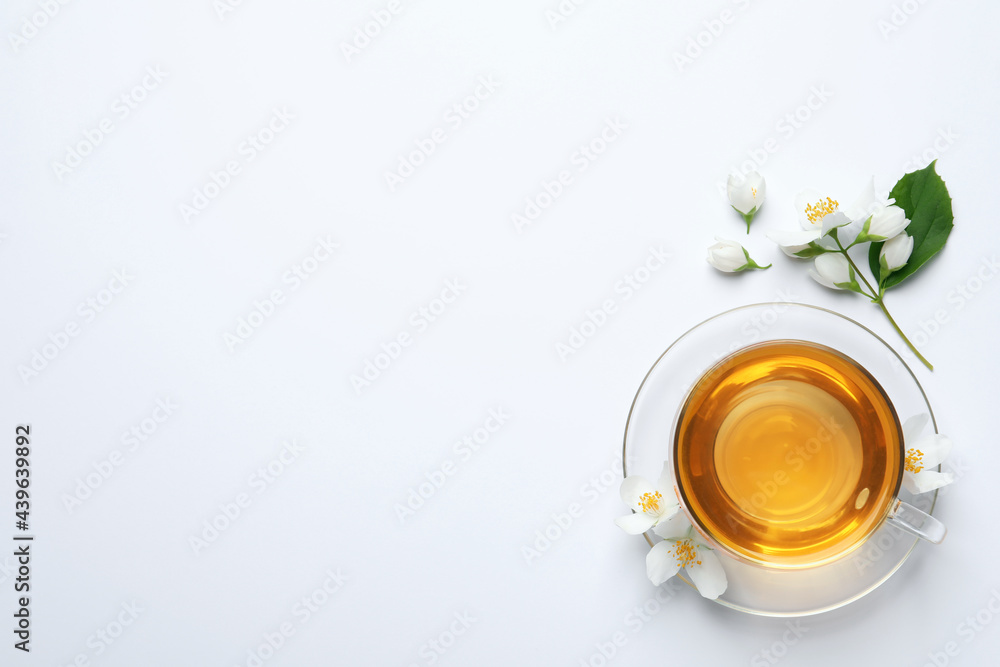 Glass cup of aromatic jasmine tea and fresh flowers on white background, top view. Space for text Glass cup of aromatic jasmine tea and fresh flowers on white background, top view. Space for text