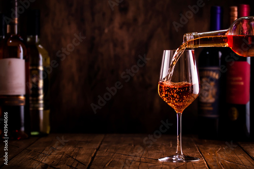 Fototapeta Naklejka Na Ścianę i Meble -  Wine tasting. Rose wine pouring into glass on wooden background with selection of red, white and rose wines in bottles