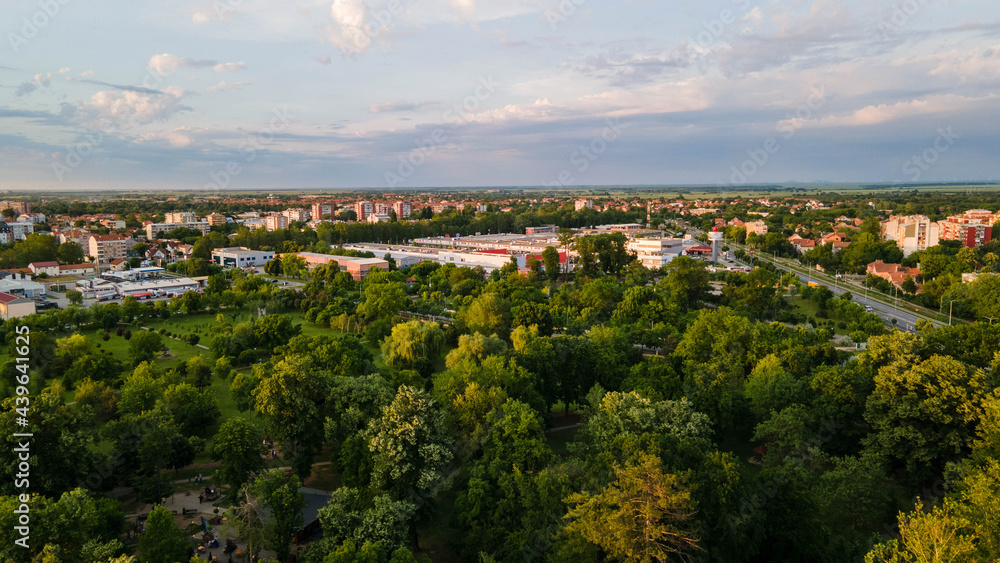 Top view aerial photo from flying drone of a city park with walking path and green zone trees in evening time. Aerial view of forest and city.