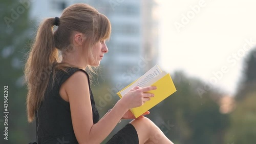 Female student sitting in summer park reading textbook outdoors. Education and sudy concept. photo