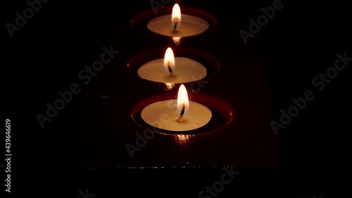 Close-up macro footage of the hand that lights tea light candles in red candle holder in the darkness.