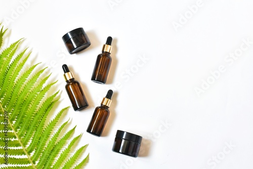 Set of eco natural cosmetics on wood podium. Bottles with pipettes with essential oil and jars of moisturizer, fern leaves on a white background. View from above. Copy space.
