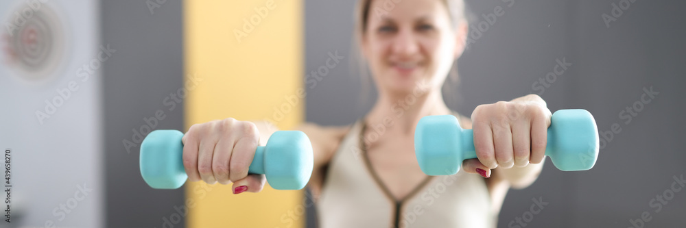 Young woman holding blue dumbbells in her hands closeup Young woman holding blue dumbbells in her hands closeup