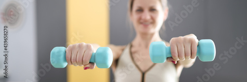 Young woman holding blue dumbbells in her hands closeup