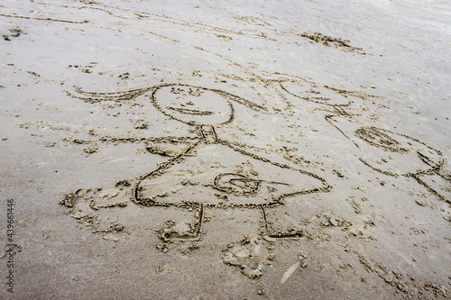 Stylized outlines of children drawn in wet grainy sand at beach.