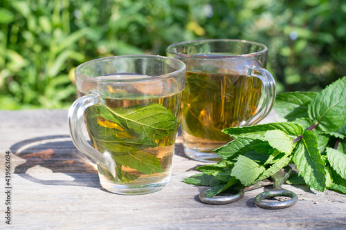 Glasses of mint tea and bundle of fresh mint on wooden table in garden