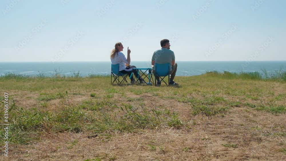 Happy couple on date admire beautiful landscape while sitting on travel chairs. Loving couple. Family travels, rests on campsite. Happy people together nearby, enjoying nature Happy couple on date admire beautiful landscape while sitting on travel chairs. Loving couple. Family travels, rests on campsite. Happy people together nearby, enjoying nature