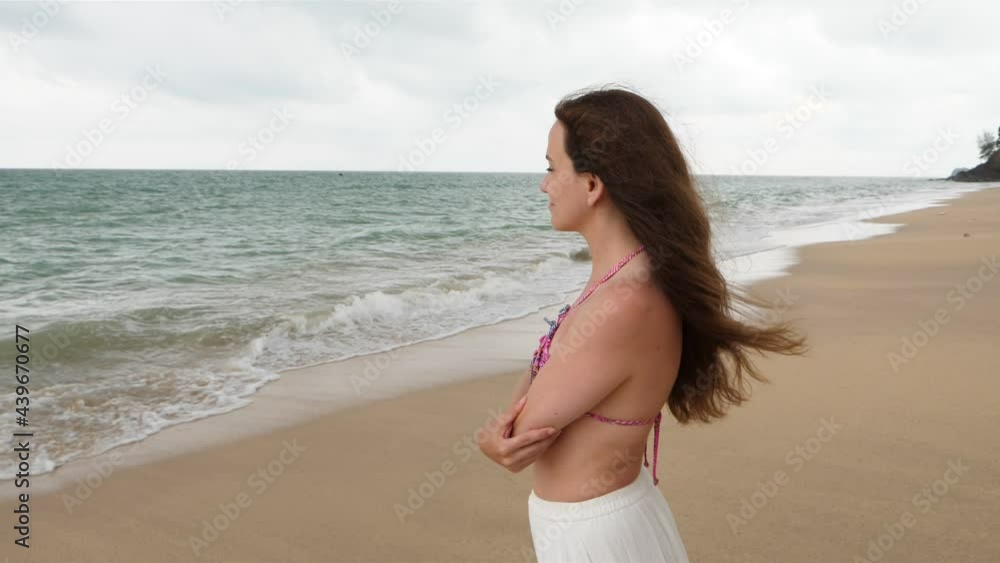 Fresh air from sea touch her face, long hair fly, dreamy mood. Woman stand at beach look at water, absorbed in thoughts. Cloudy and warm weather at tropical island of Thailand Fresh air from sea touch her face, long hair fly, dreamy mood. Woman stand at beach look at water, absorbed in thoughts. Cloudy and warm weather at tropical island of Thailand
