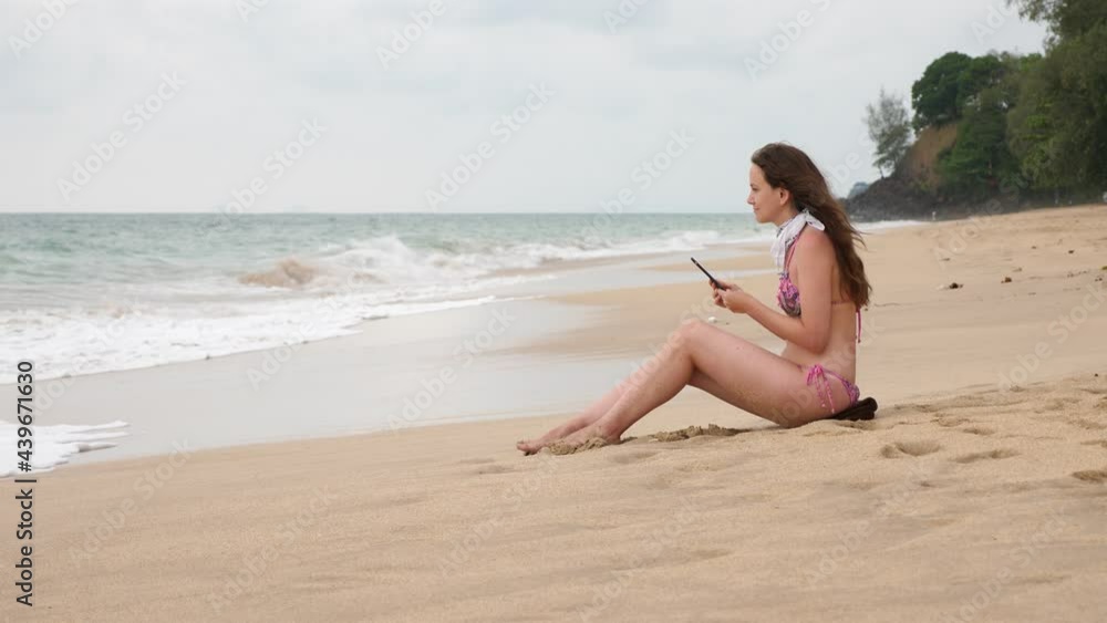 Woman sit on beach, look to tropical sea, windy and cloudy weather. Big wave break down and water uprush and reach her. She did not expect this, funny and emotional scene Woman sit on beach, look to tropical sea, windy and cloudy weather. Big wave break down and water uprush and reach her. She did not expect this, funny and emotional scene