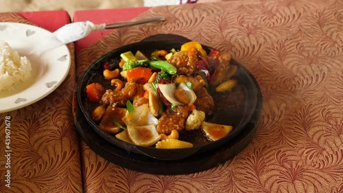 Cashew chicken meal served on hot iron pan, continue to frizzle on the table, food broil with vapor. Close up shot of popular Thai meal, Kai Phat Met Mamuang, served at affordable restaurant photo