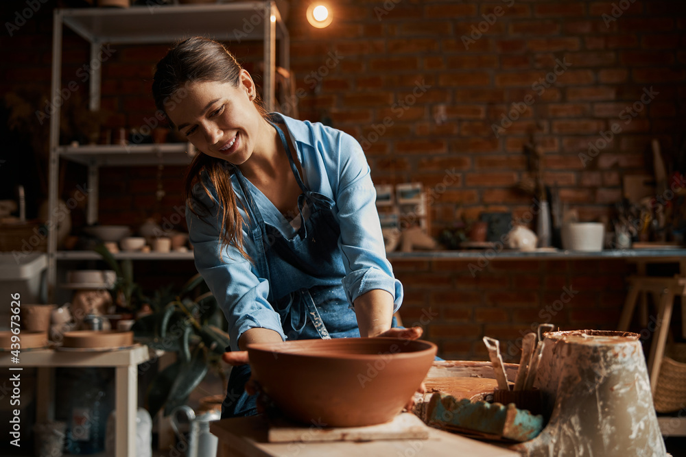 Gorgeous attractive caucasian craft woman holding ceramic non painted bowl in hand in pottery workshop