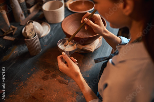 Beautiful elegant woman designer in apron during process making tableware in pottery workshop