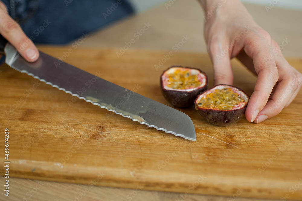 Female hands is cutting a fresh ripe passion fruit, maracuya on a cut wooden board. Exotic fruits, healthy eating concept