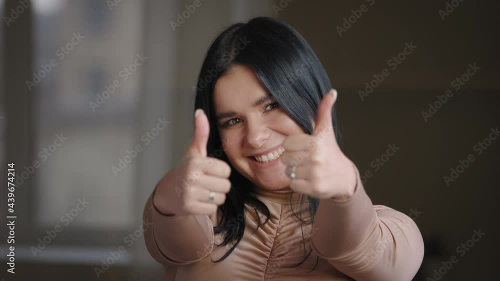 Portrait ethnic mexican spanish brazilian woman millennial brunette plus size model posing looking at camera alone indoor, showing approval gesture. Close-up plump happy girl puts thumbs up makes like Portrait ethnic mexican spanish brazilian woman millennial brunette plus size model posing looking at camera alone indoor, showing approval gesture. Close-up plump happy girl puts thumbs up makes like