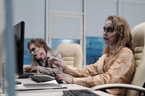 Ugly zombie female sitting in armchair in front of computer monitor