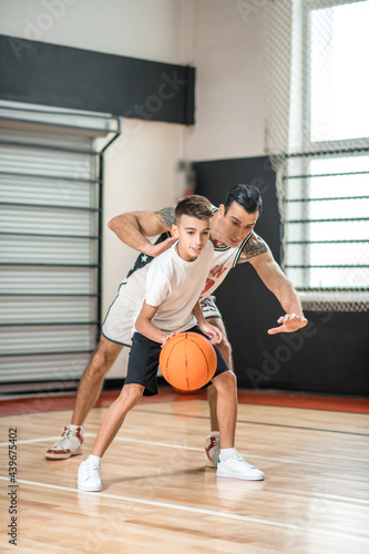 Dark-haired man playing basketball with a boy