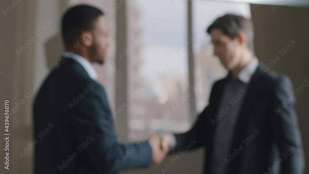 Blurred two multiracial multinational businessmen talking in office shaking hands, unfocused view male silhouettes afro american man and caucasian manager conclude agreement union handshake, teamwork Blurred two multiracial multinational businessmen talking in office shaking hands, unfocused view male silhouettes afro american man and caucasian manager conclude agreement union handshake, teamwork