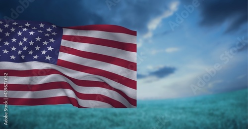 Composition of american flag billowing over blue ocean cloudy blue sky