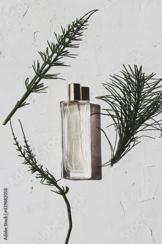 Minimalistic design for fresh nature scented perfume advertising. A clear glass bottle of perfume on a white background with two green leaves. 