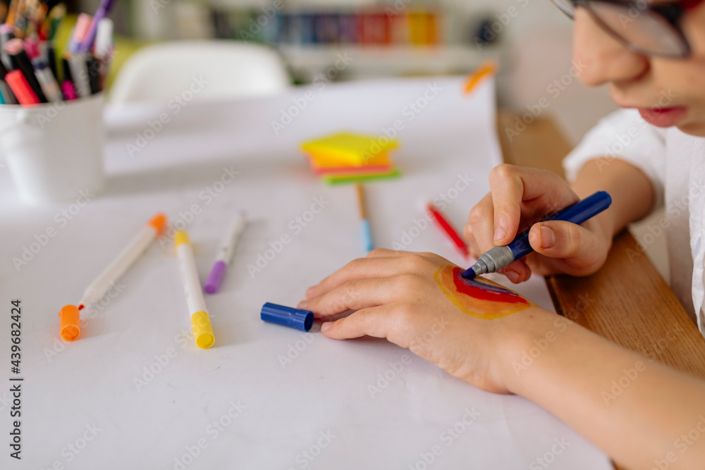 Cropped view of pre-teen boy drawing on his hand a rainbow with markers Cropped view of pre-teen boy drawing on his hand a rainbow with markers