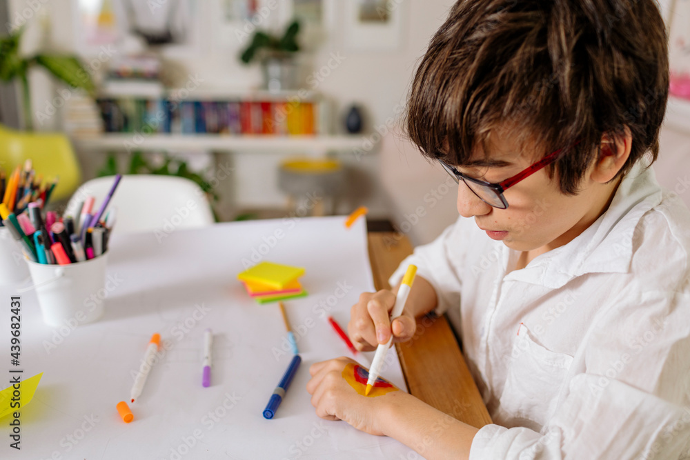 Cropped view of pre-teen boy drawing on his hand a rainbow with markers Cropped view of pre-teen boy drawing on his hand a rainbow with markers