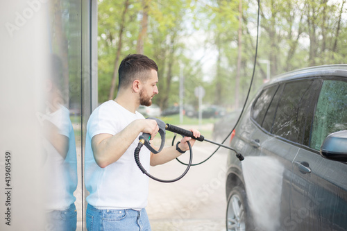 Car washing. Man cleaning car using high pressure water.