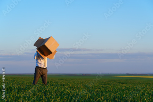businessman puts his head in a cardboard box and poses on a green grass field - business concept