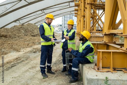 Three builders discussing blueprint at construction site