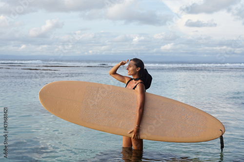 Girl in with a surfboard looks at the ocean and waves. Surfer girl photo