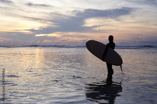 Silhouette of a girl with a surf at sunset by the ocean. Surfer girl