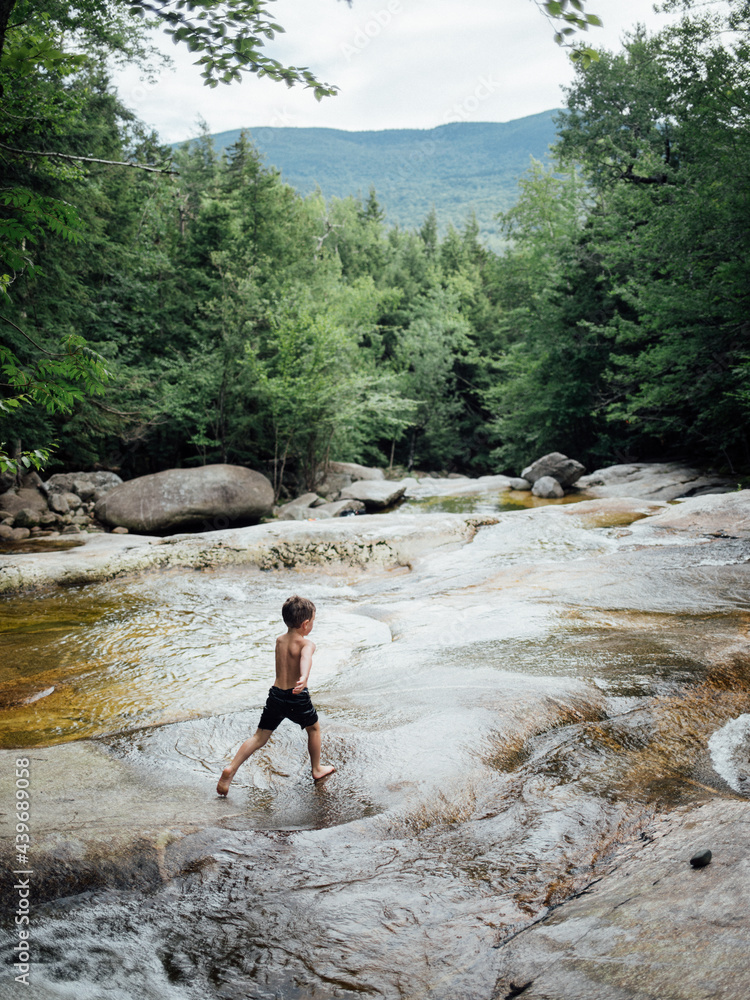 A young boy runs across rocks while playing in a mountain stream. A young boy runs across rocks while playing in a mountain stream.