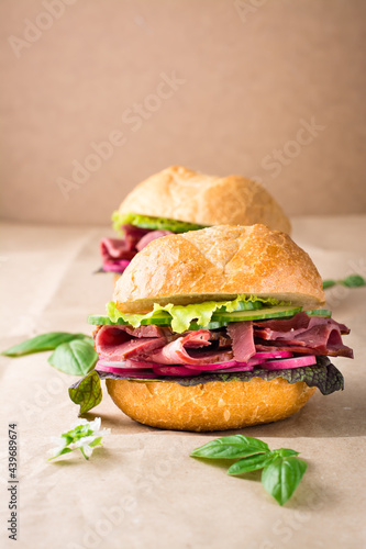 Fresh hamburger with pastrami, cucumber, radish and herb on craft paper. American fast food. Vertical view. Copy space