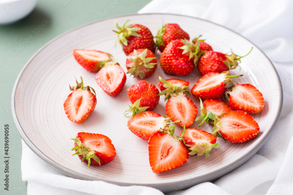 Fresh whole and sliced strawberries on a plate on a green background. Summer vitamin food. Close-up