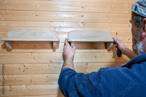 hands of a master carpenter attach a wooden shelf to the wall. Production of handmade furniture to order and its installation
