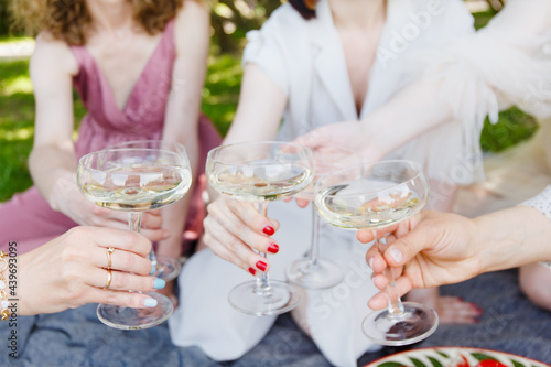 
A picnic, a meeting of girls or a bachelor party in a beautiful blooming garden in spring. Girls in light dresses drink champagne and eat pizza in the park