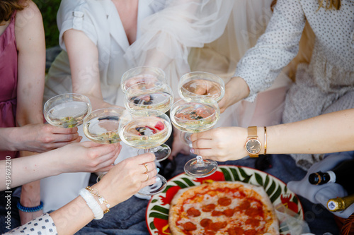 A picnic, a meeting of girls or a bachelor party in a beautiful blooming garden in spring. Girls in light dresses drink champagne and eat pizza in the park	