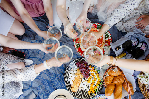 
A picnic, a meeting of girls or a bachelor party in a beautiful blooming garden in spring. Girls in light dresses drink champagne and eat pizza in the park