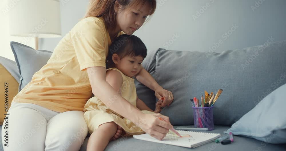 Happy cheerful Asia family mom teach girl paint use album and colourful pencils having fun relax on couch in living room at house. Spending time together, Social distance, Quarantine for coronavirus. Happy cheerful Asia family mom teach girl paint use album and colourful pencils having fun relax on couch in living room at house. Spending time together, Social distance, Quarantine for coronavirus.