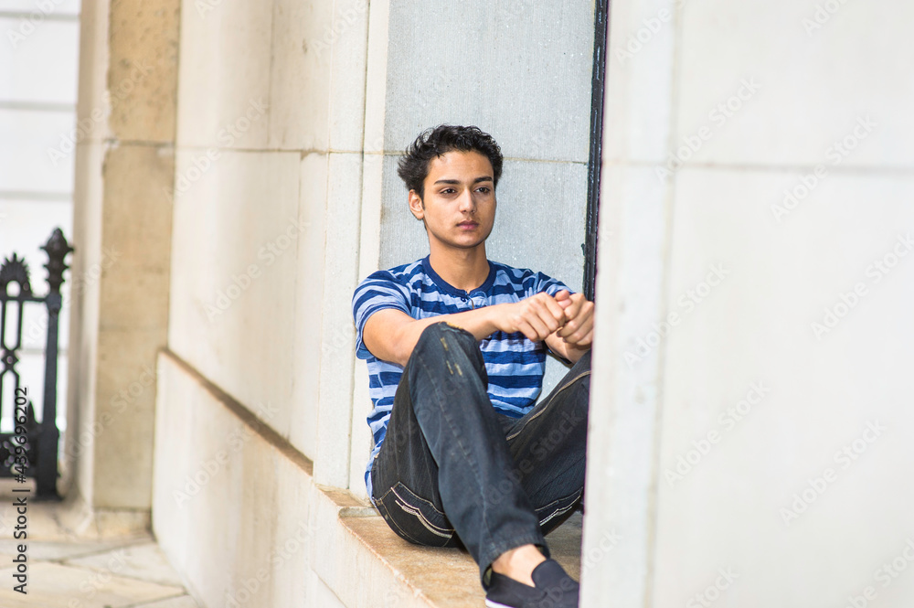 Dressing in a blue lines T shirt and black pants, a young asian teenager is sitting on a window and into deeply thinking. Dressing in a blue lines T shirt and black pants, a young asian teenager is sitting on a window and into deeply thinking.