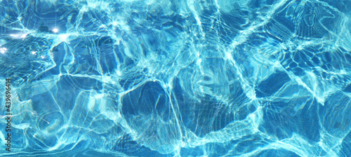 Blue rippled water surface of turquoise swimming pool. Summer vacations resort concept. Background of water ripple under bright sunny sky. Full frame texture. Banner with place for text.