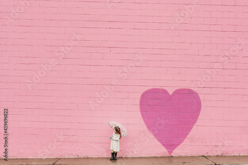 Environmental portrait of little girl in front of pink wall photo