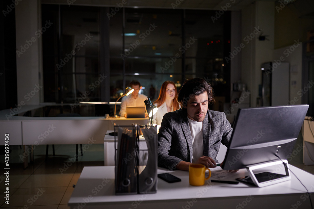 Team of managers office workers working on project very late, using computer. Hardworking people in formal wear engaged in work, thinking, brainstorming, be in time for deadline. copy space