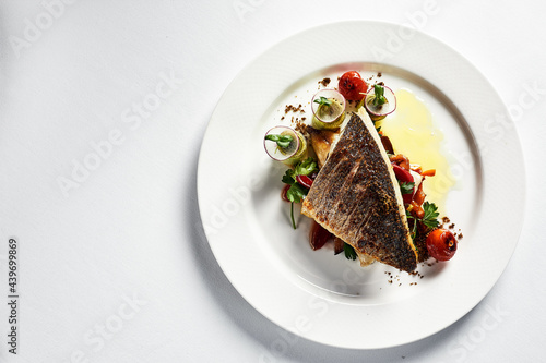 Grilled seabass with vegetables top view, close-up, white plate, light background, copy space