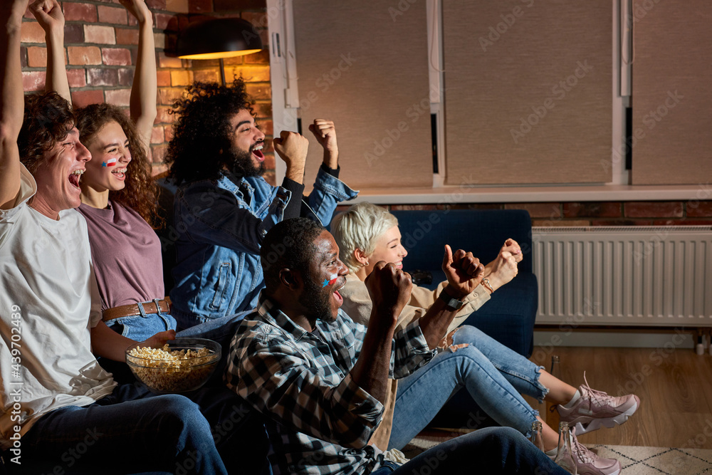 Young people watching big game, cheering for best team. Sport,people, leisure, friendship and happiness concept. At home in the evening or night, cheerful guy and ladies celebrating win