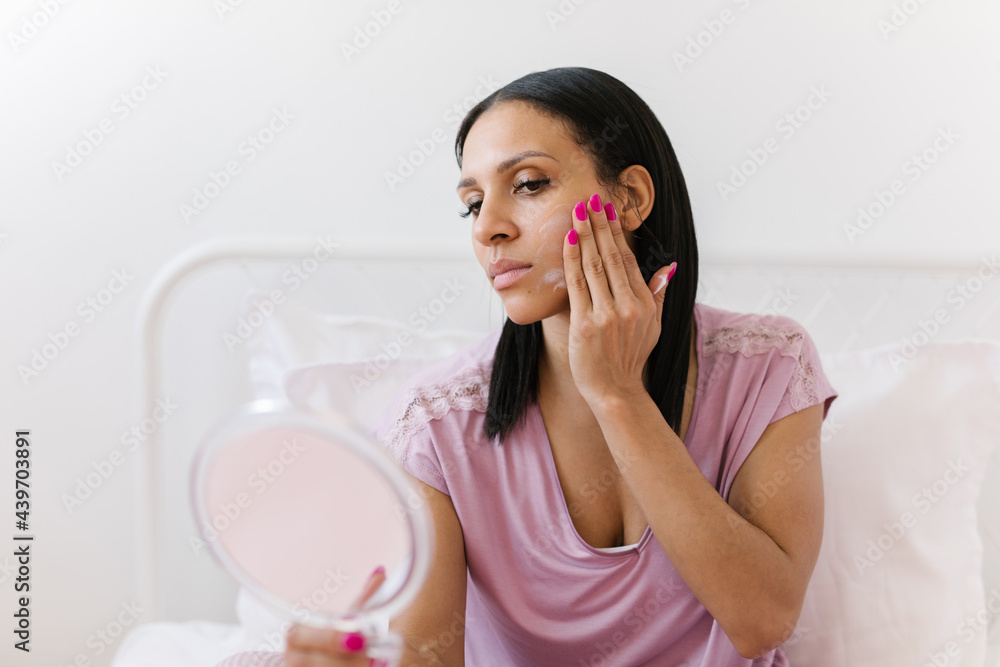Beautiful black woman applying facial lotion while looking in the mirror Beautiful black woman applying facial lotion while looking in the mirror