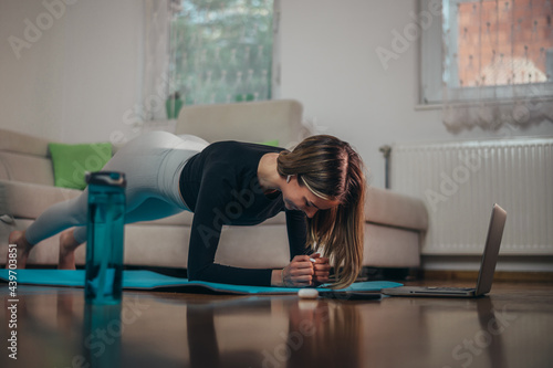 Young attractive woman in a plank position using a laptop while training at home