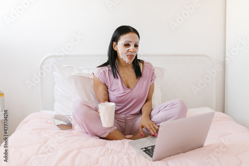 Morning routine. Woman drinking mornin coffee and using laptop while doing a beauty treatment  photo