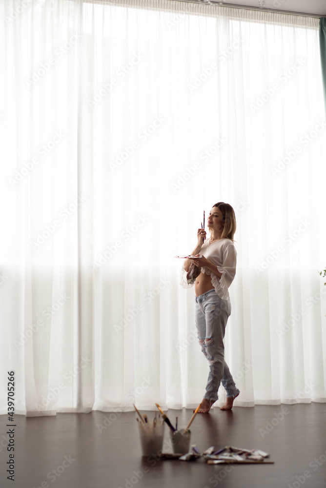 Pregnant female artist posing in front of window and painting with oil paint Pregnant female artist posing in front of window and painting with oil paint